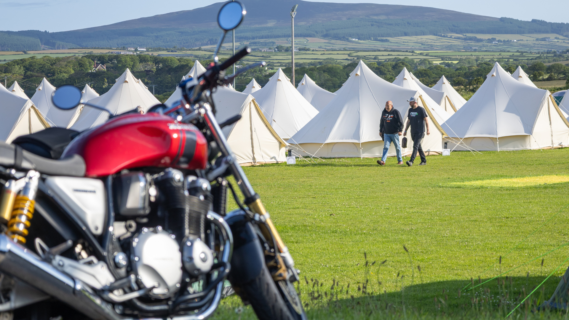 A motorbike in front of a field of bell tents, as part of a glamping site for the TT races accommodation