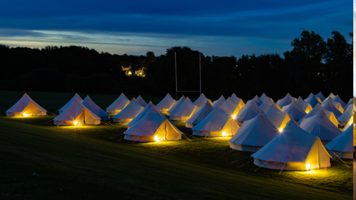 A field of glamping bell tents lit up at night under a dark sky.