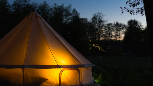 Lit-up bell tent glowing at night in a glamping village.